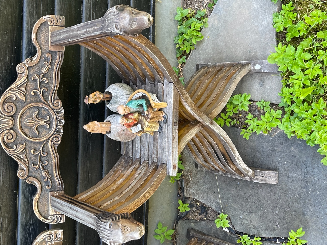 Keramikprydnad med ett äldre par på en parkbänk, stående på en äldre trästol med lejonhuvuden på armstöden.
