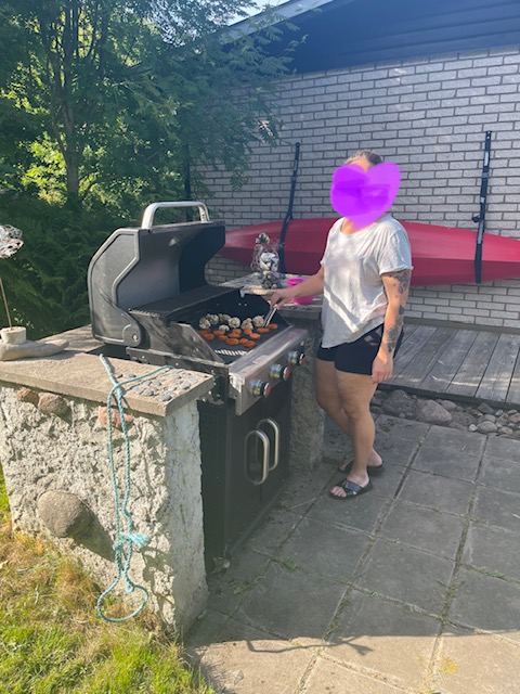 En kvinna står vid en gasolgrill, ett hjärta täcker ansiktet